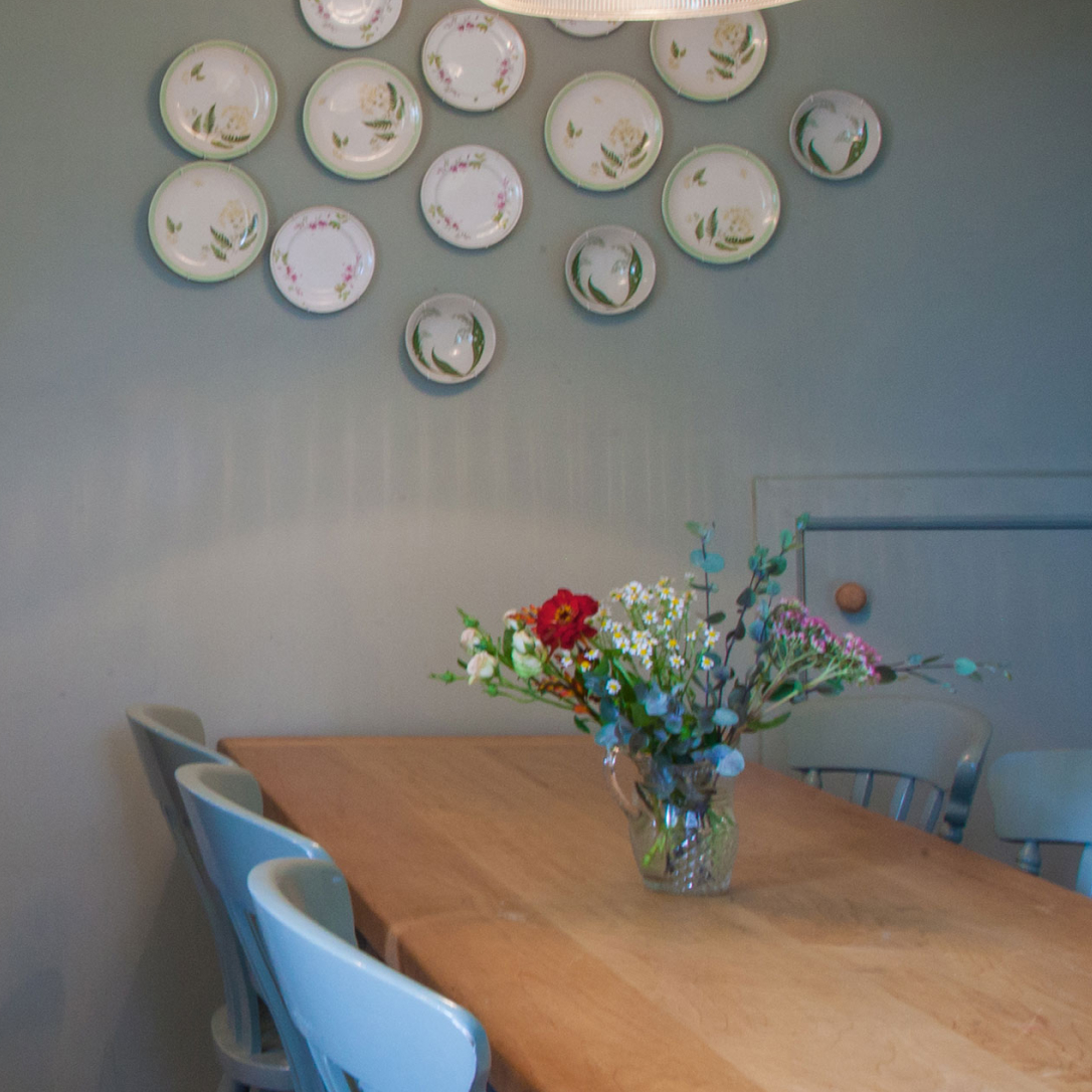 A dining table with many plates mounted on the wall behind it.