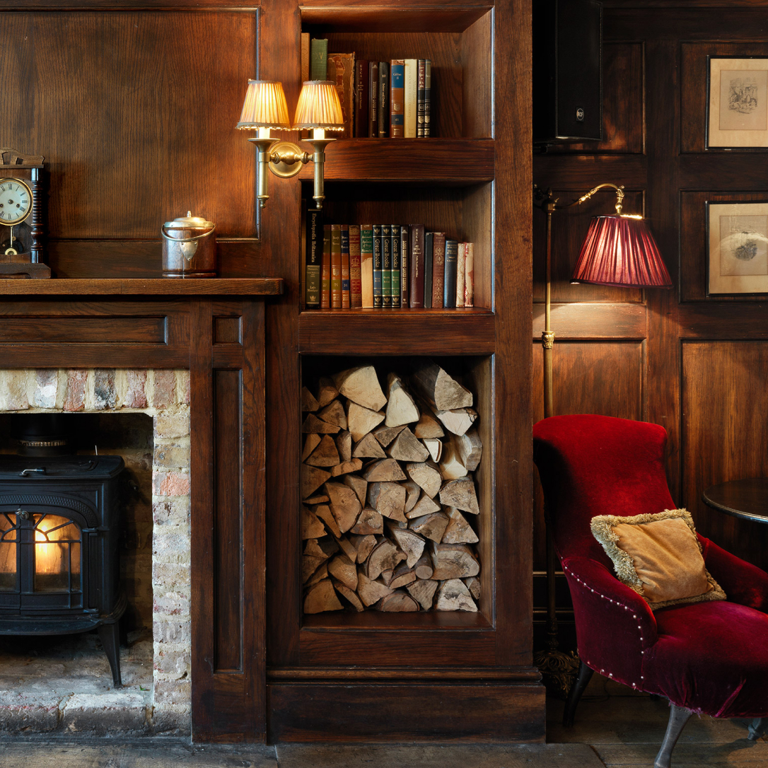 A wood panelled room with a fireplace an armchair and books on shelves.