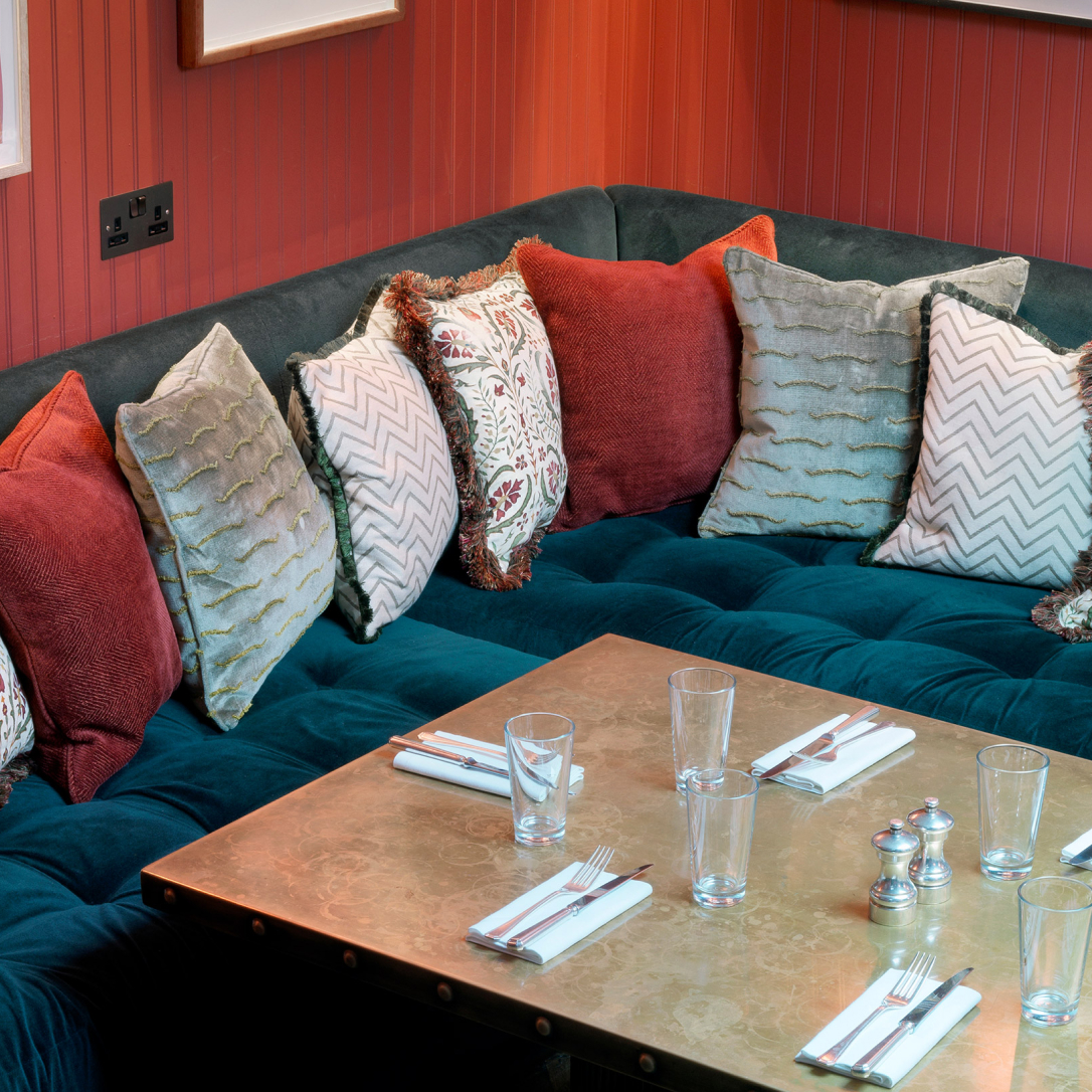 A cosy space with a table, seating and cushions.