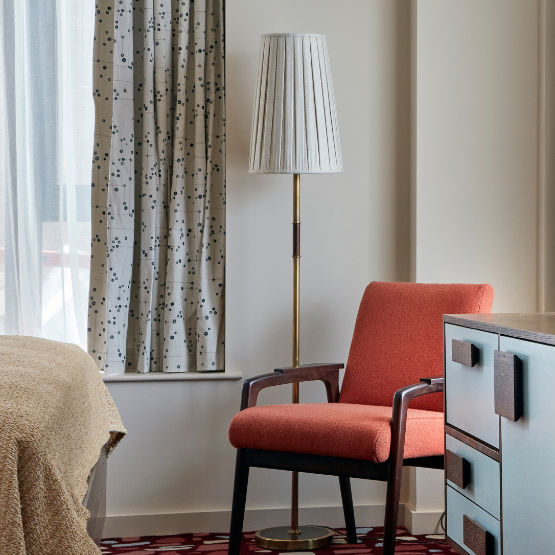 The corner of a bedroom with a chair and a floor lamp.