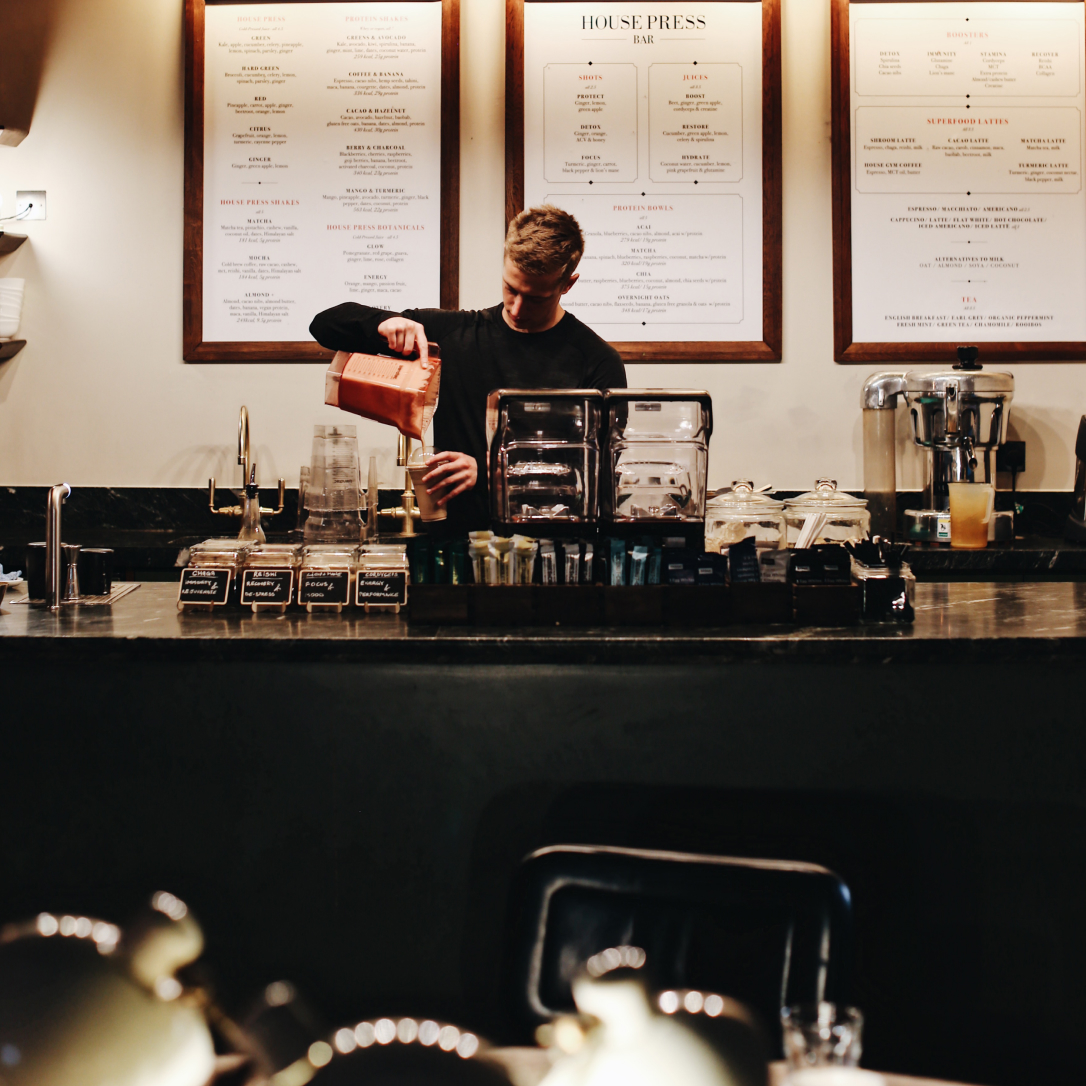 A man pours a smoothie into a glass behind a bar.
