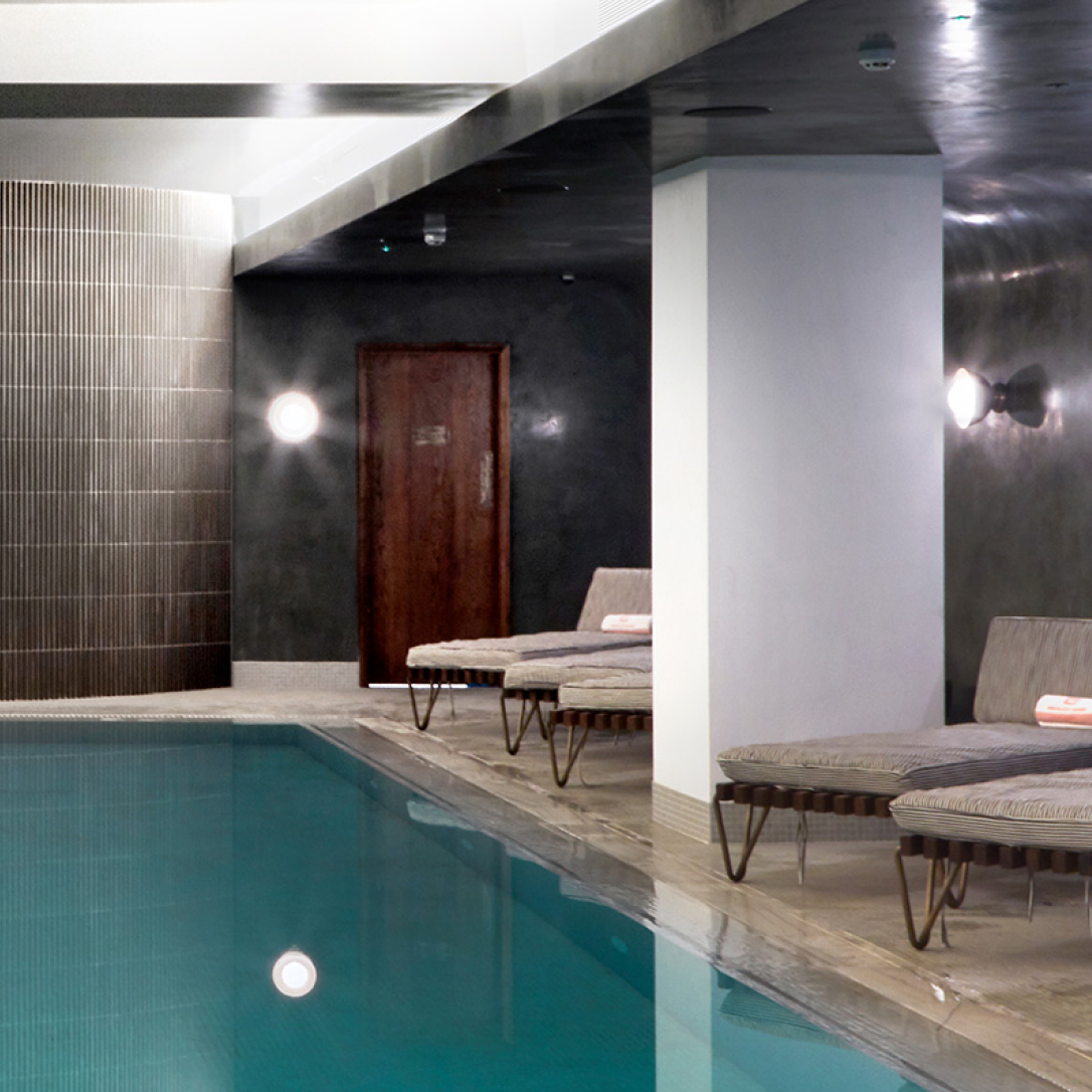 The corner of an indoor pool with loungers by the side of it.