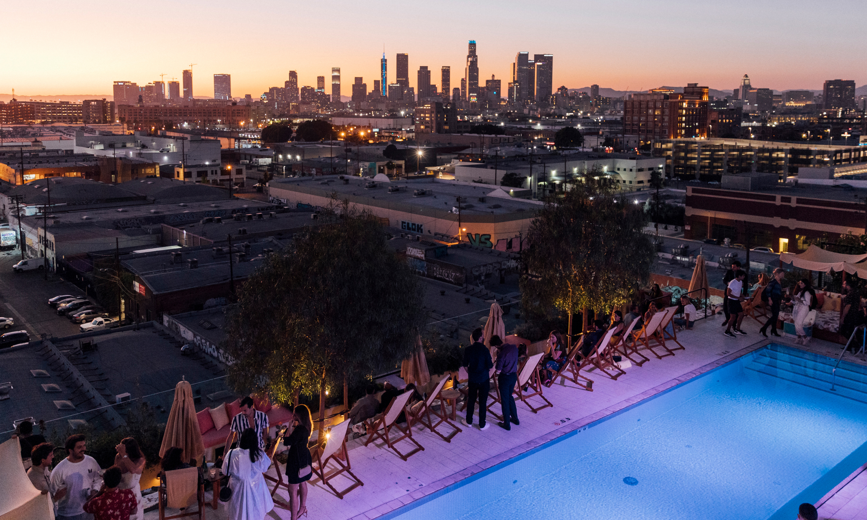 A group of people by a rooftop pool at night with a city in the background.
