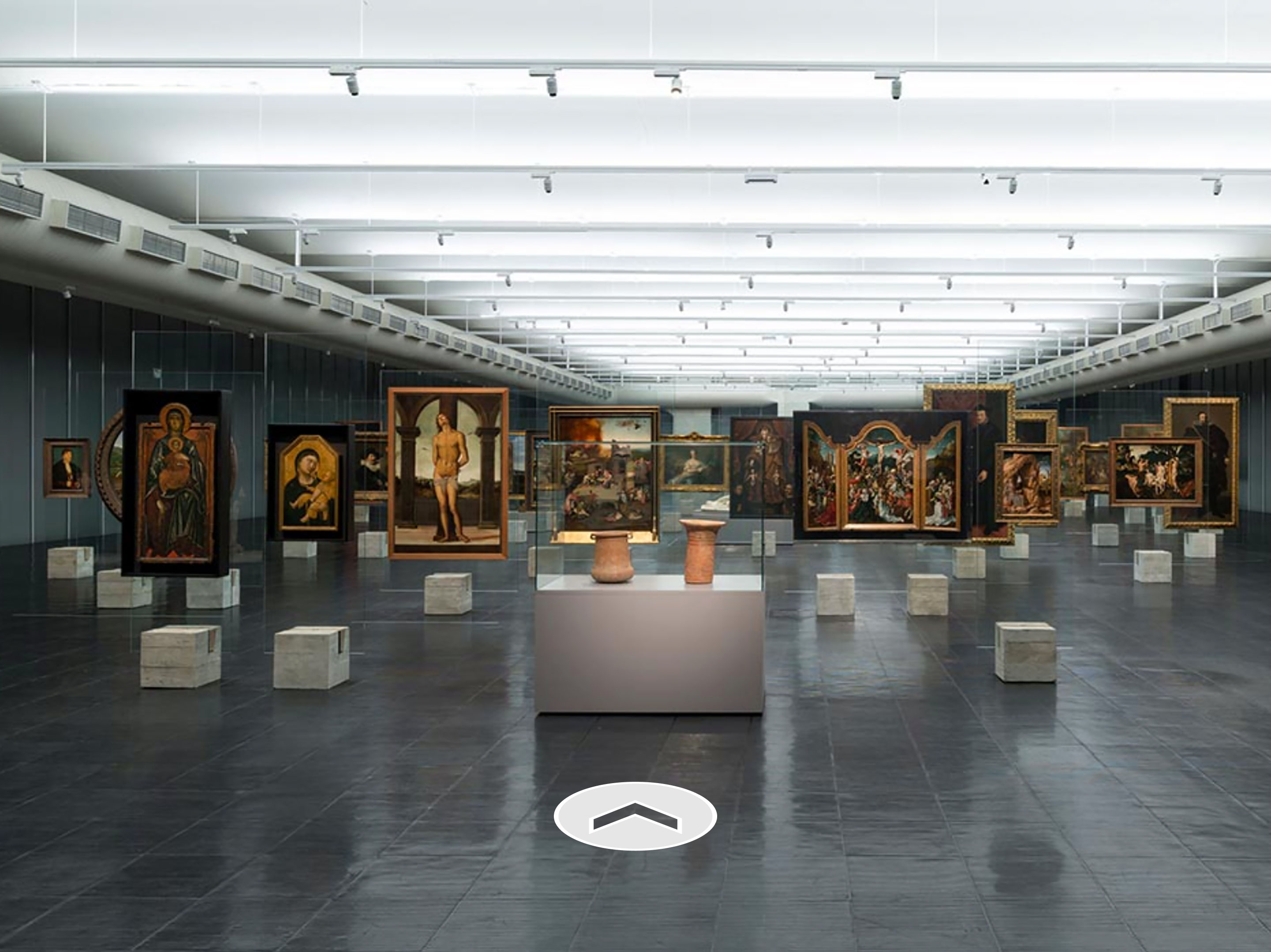 Various paintings lined up in a wide gallery space with a direction arrow at the bottom.