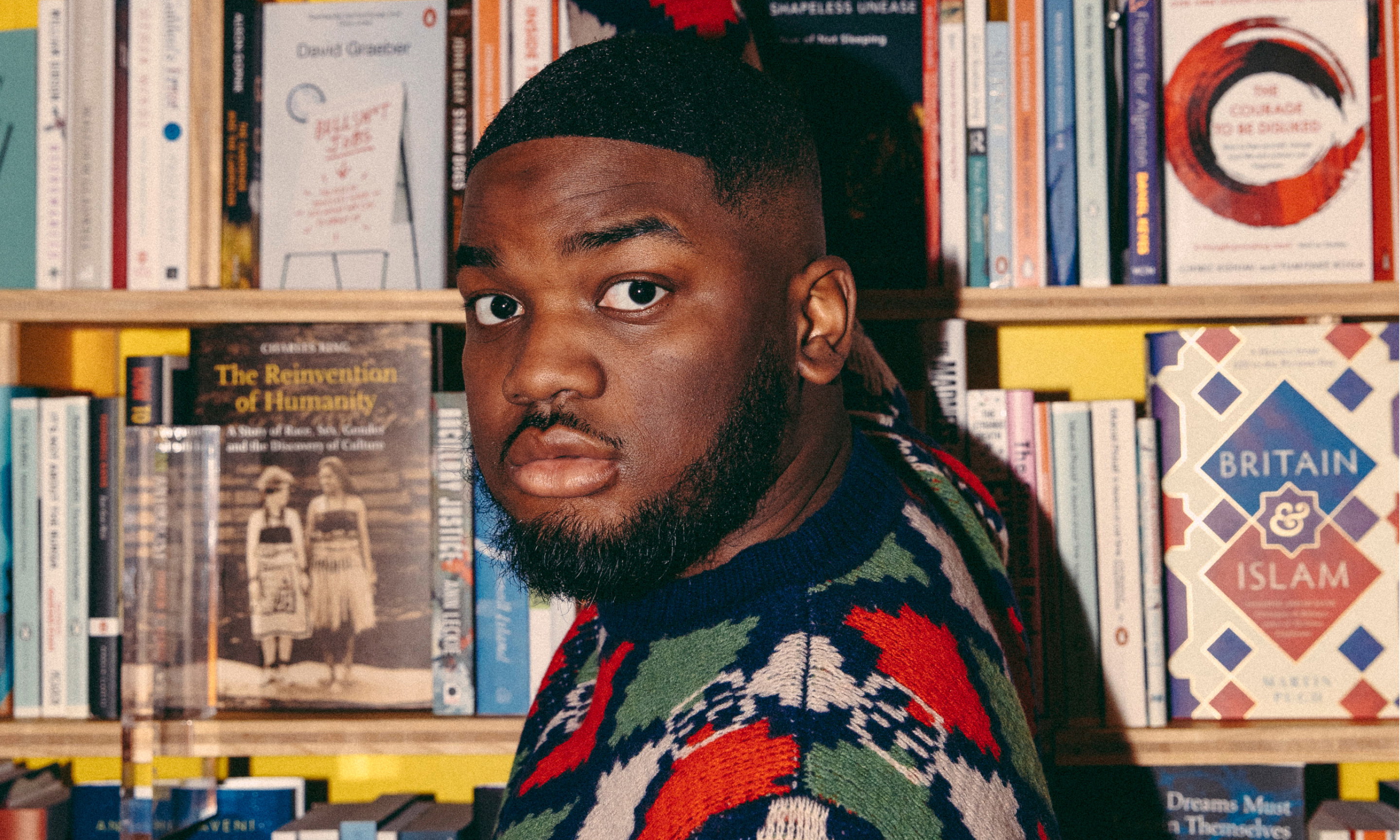 A man standing by a yellow bookcase full of books.