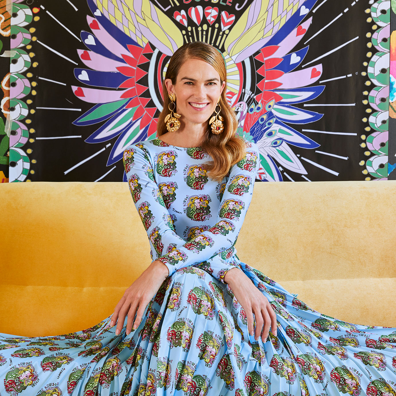 A woman in a blue print dress sitting on a yellow sofa.
