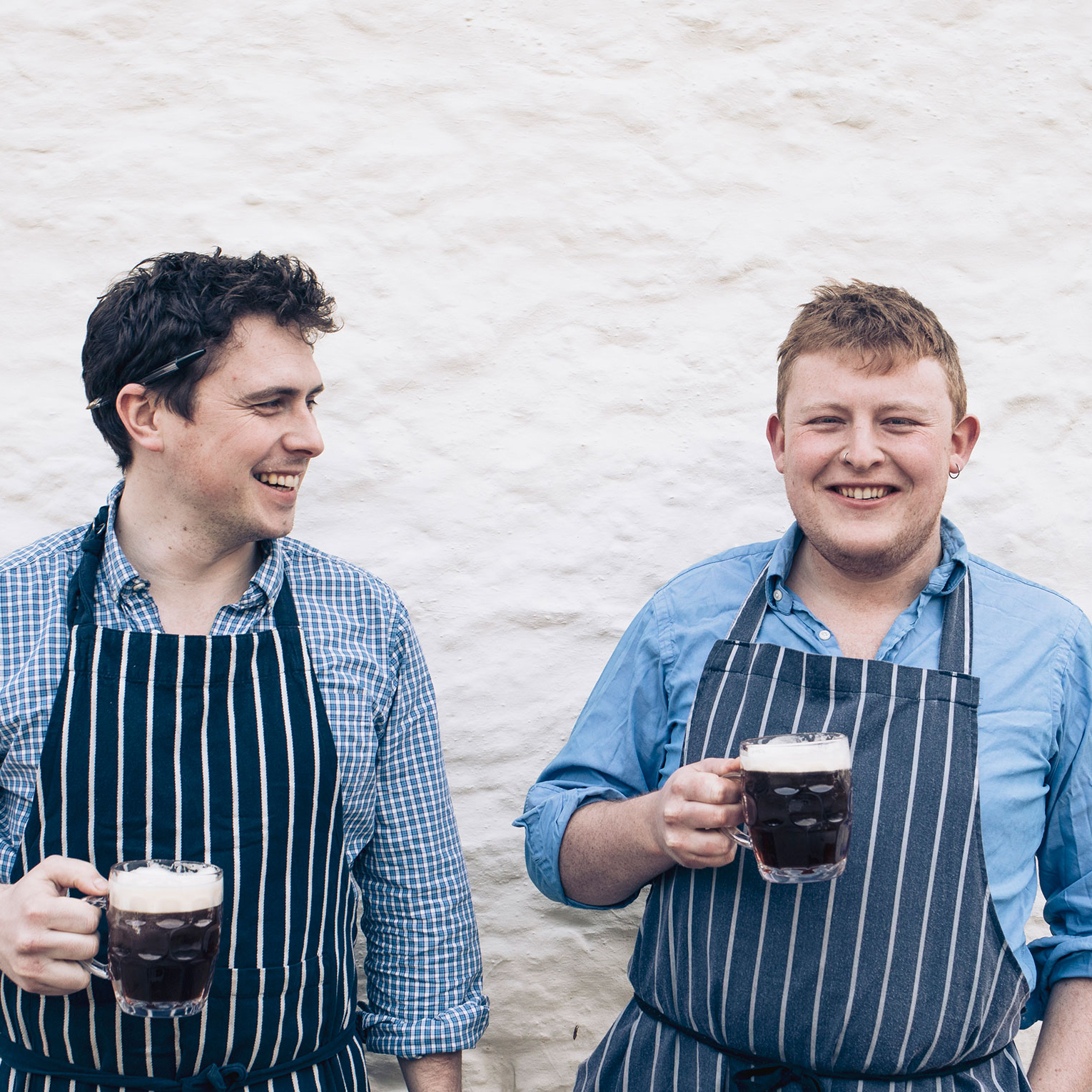 two men holding beers in aprons