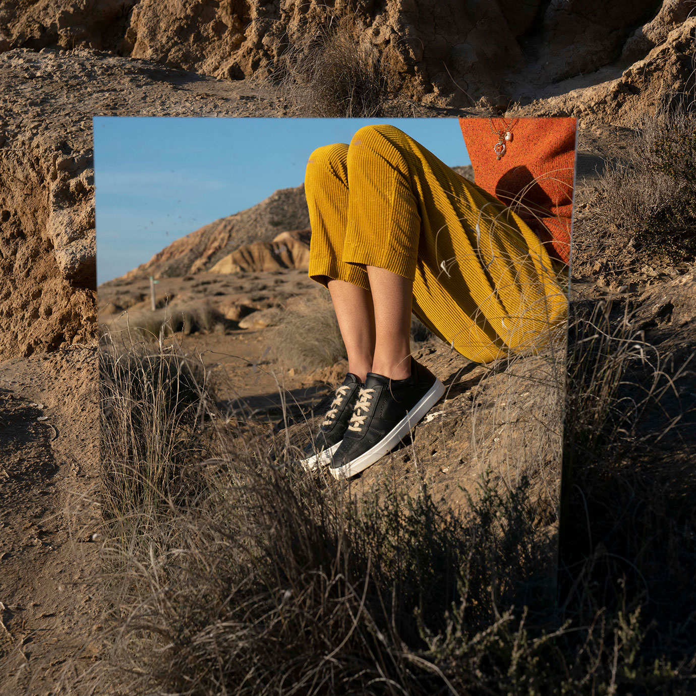 A man and shoes reflected in a mirror in the desert.