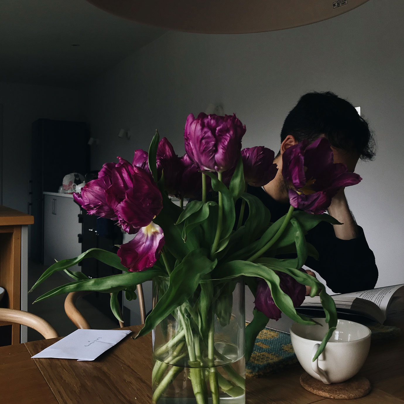 A vase of purple flowers with a person behind them.