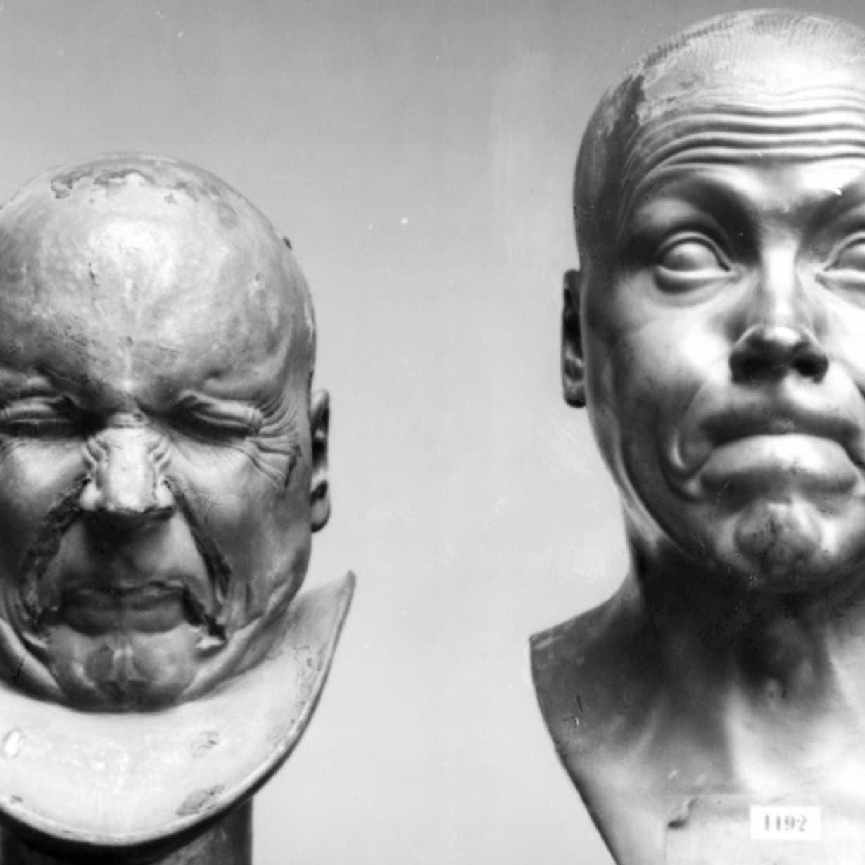 Two metal busts of a man pulling funny faces.