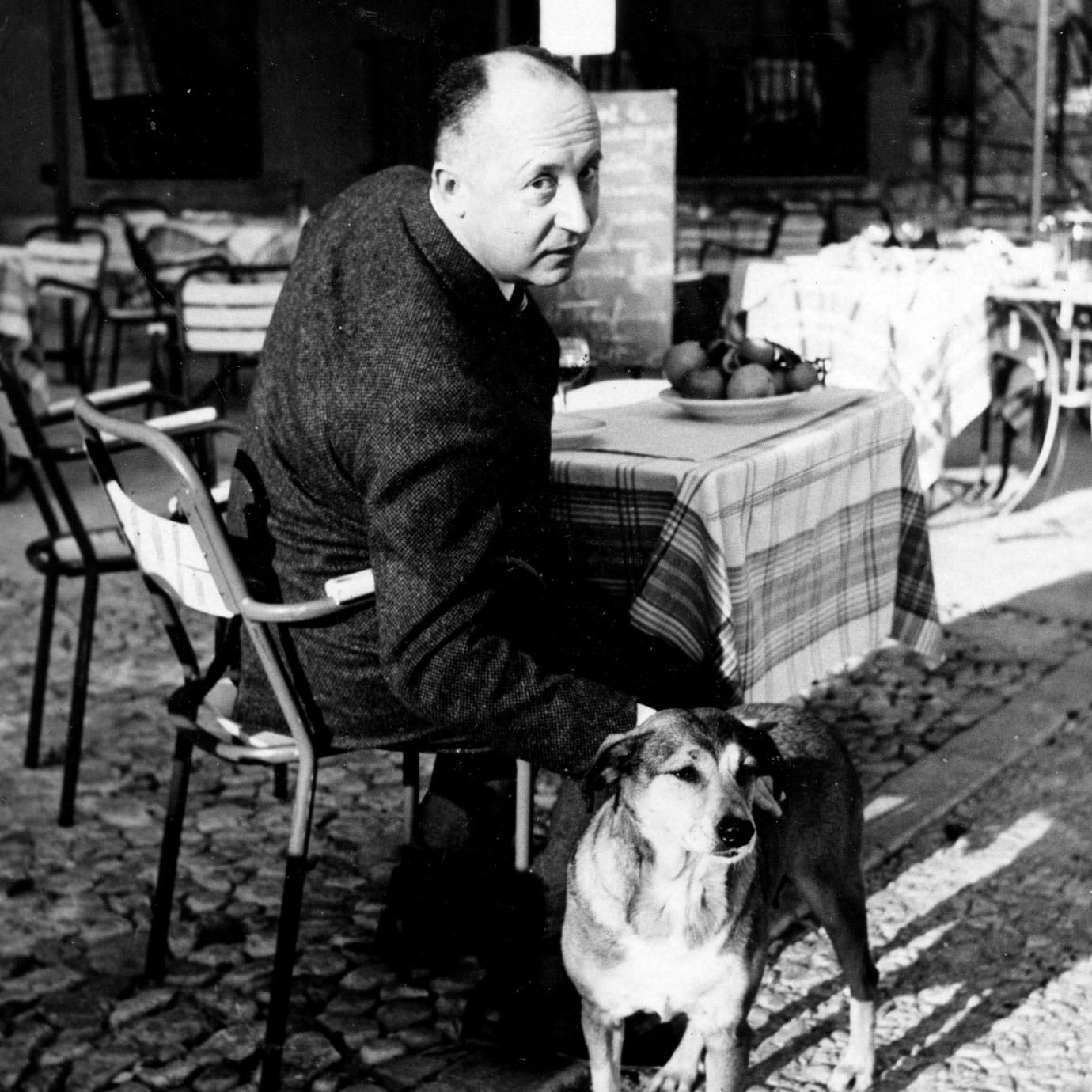 A man patting a dog while sat at an outside restaurant table.