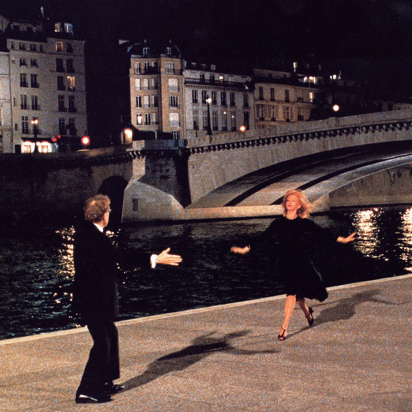 A man and a woman dancing at night by a canal and bridge.