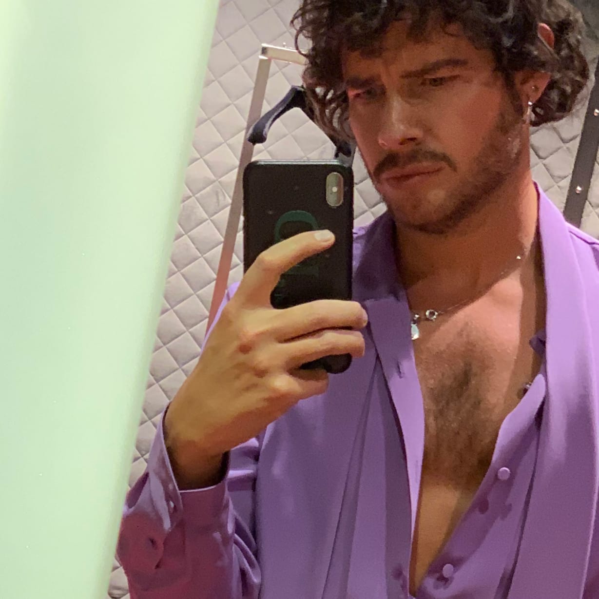 A man wearing purple clothes taking a selfie in a mirror.