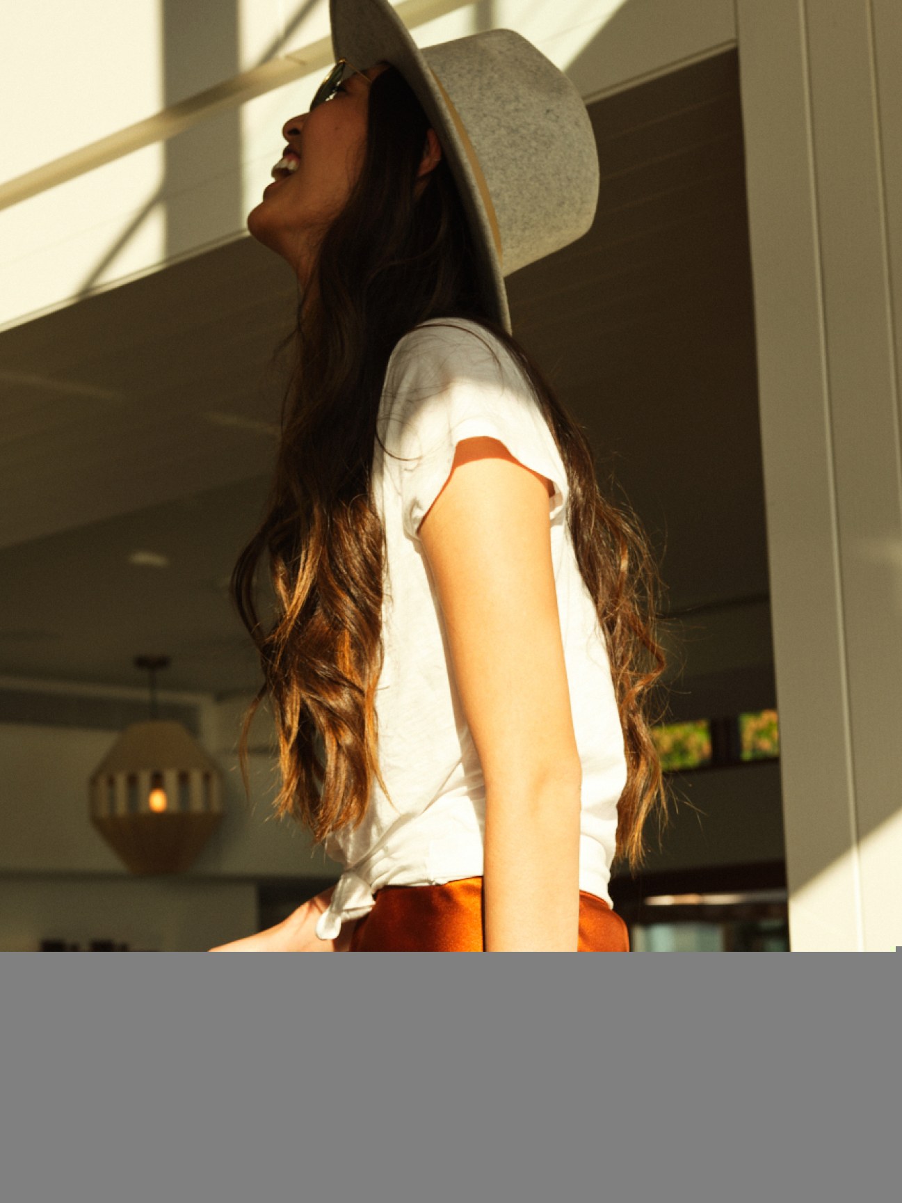 A woman in an orange skirt and a hat laughing at something.
