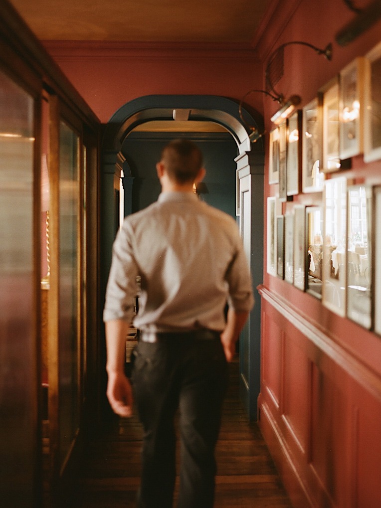 A man walks down a red corridor with artworks on the walls.