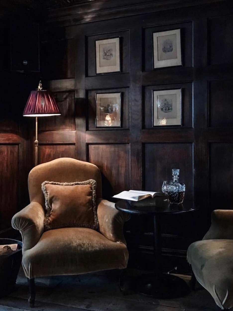 A corner of a wood panneled room with a floor lamp and an armchair.