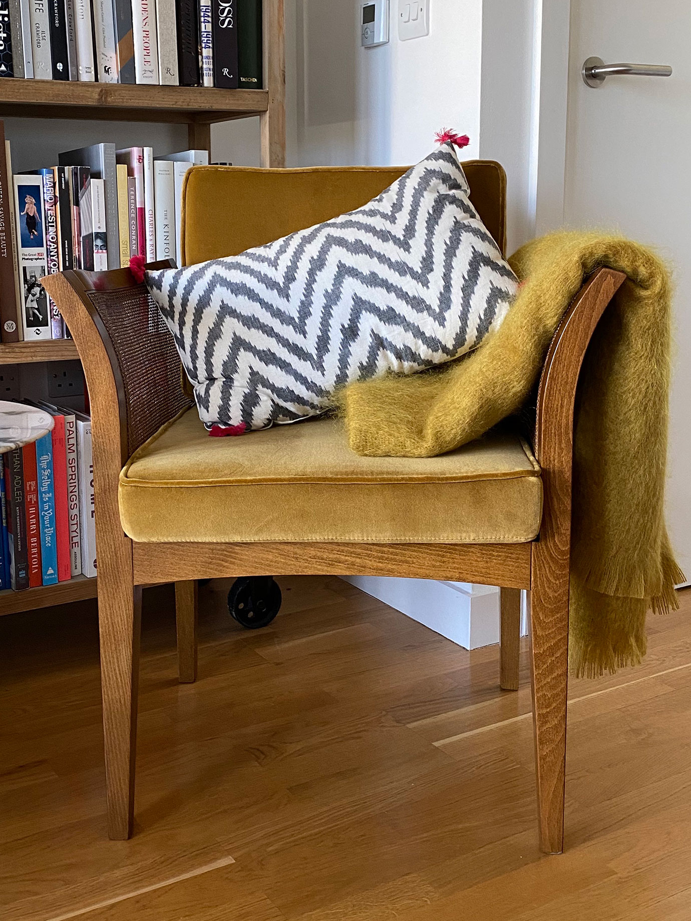 A wooden chair with a cushion and a throw on it.