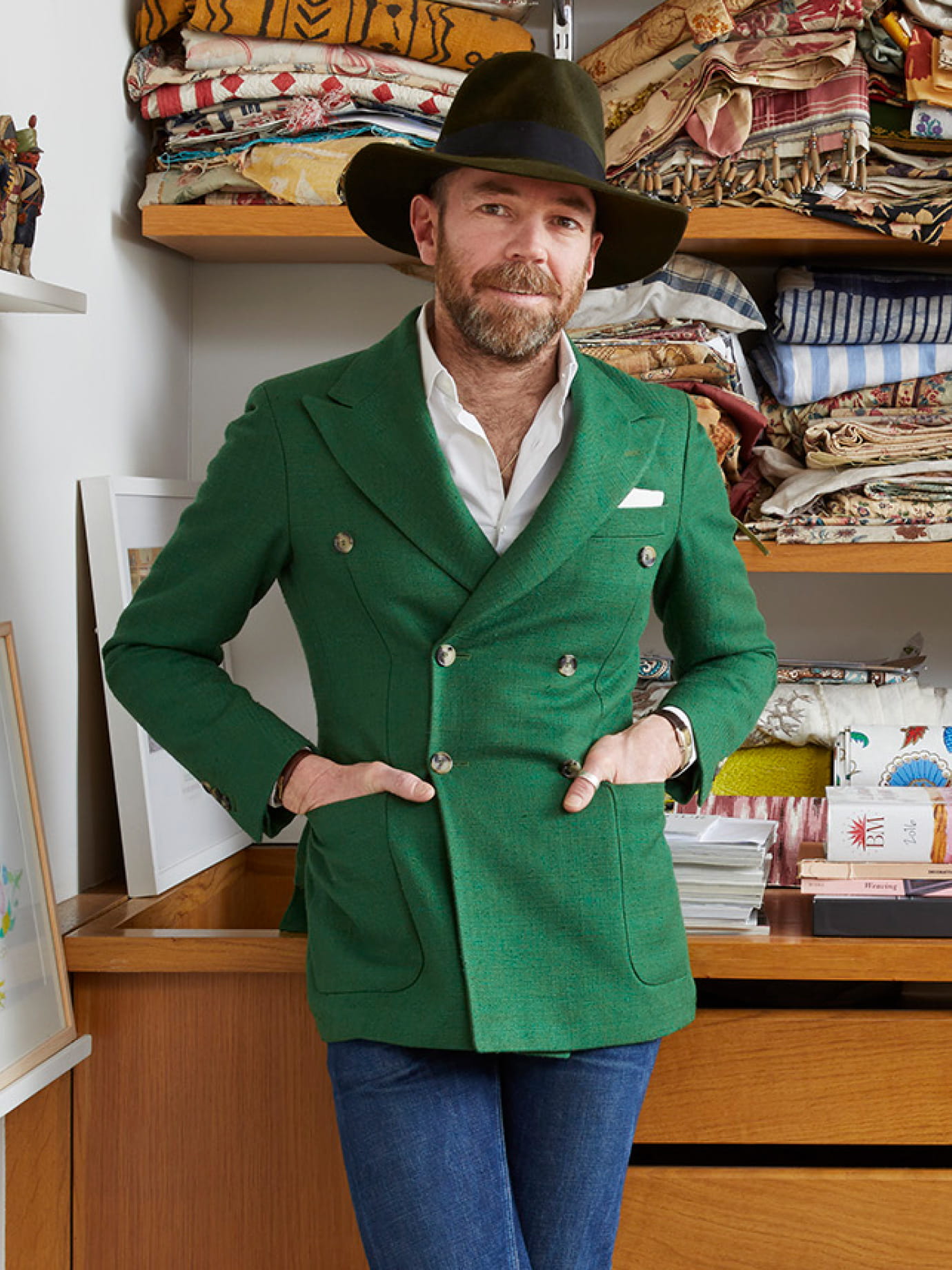 A man in a broad hat and green jacket leaning against a cabinet containing swatches.