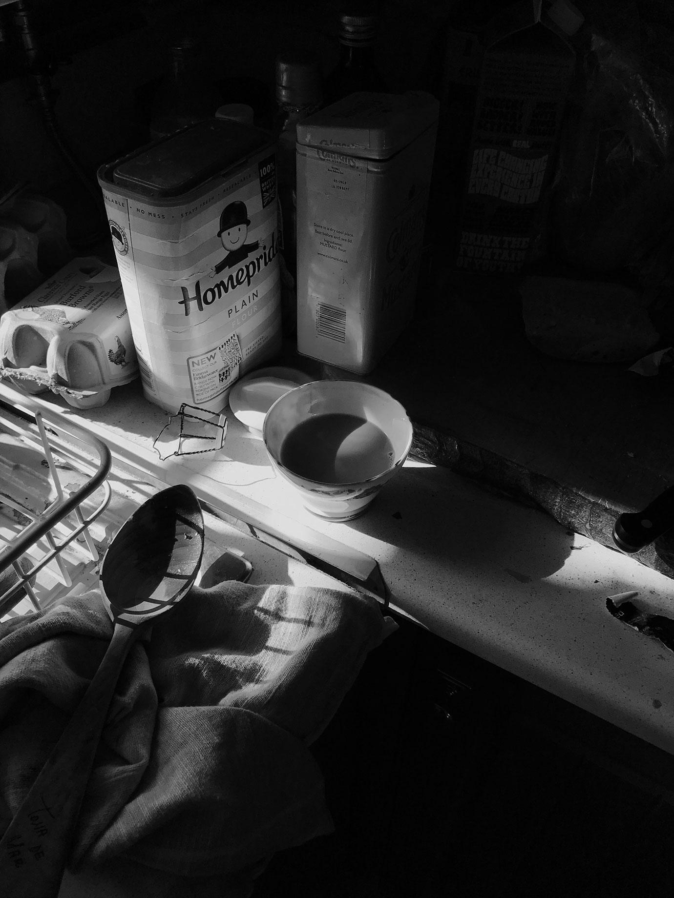 A messy kitchen surface with a cup of tea.