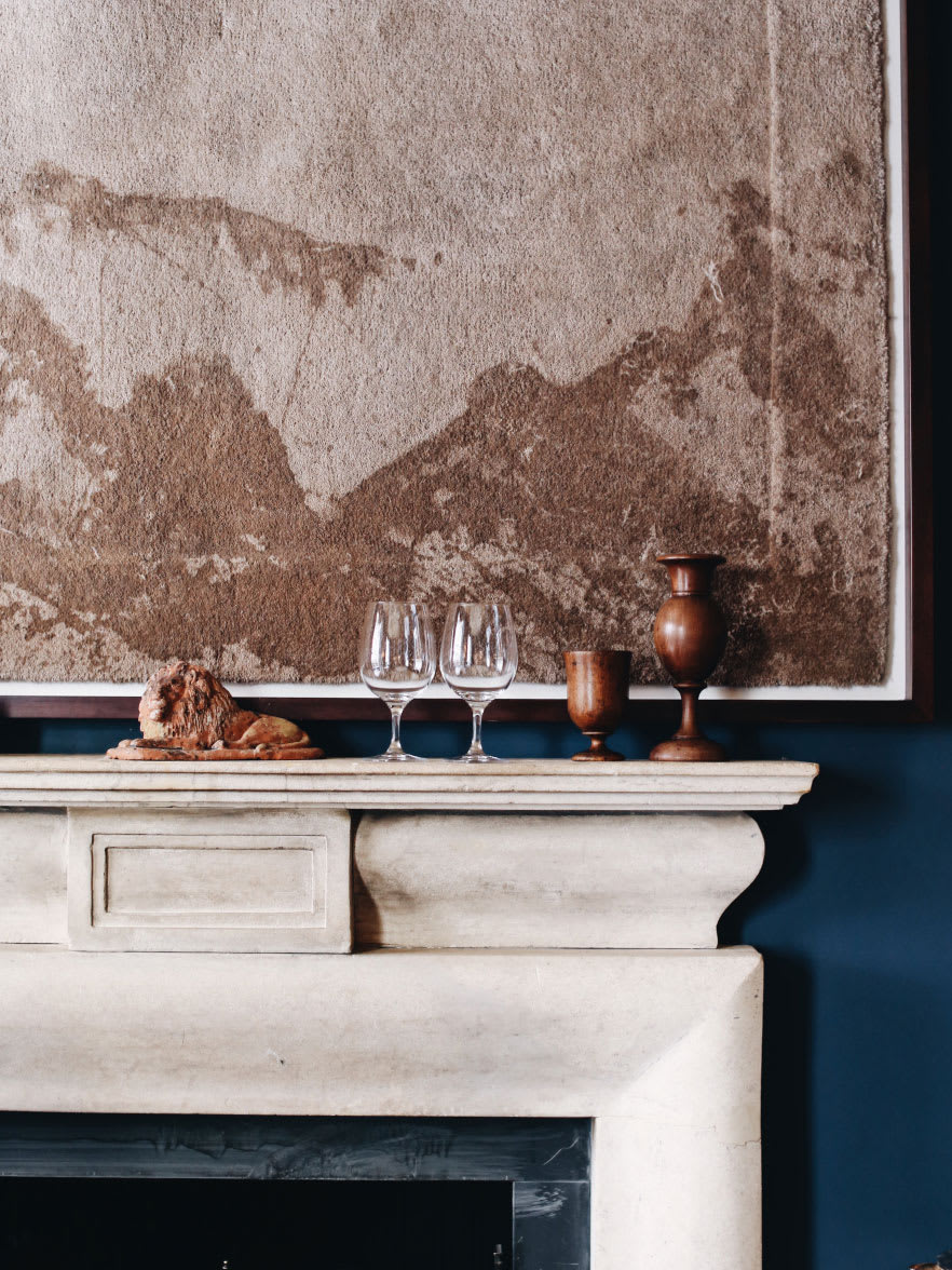 A fireplace mantle with art work on the blue wall above it.