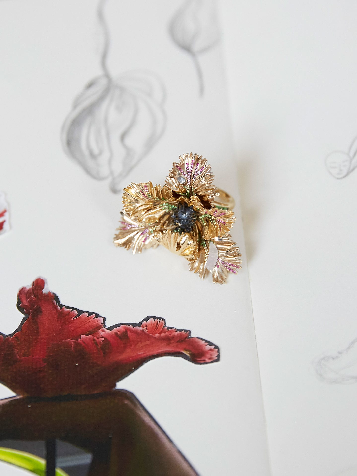 A sketch book with designs and a piece of gold jewellery resting on it.