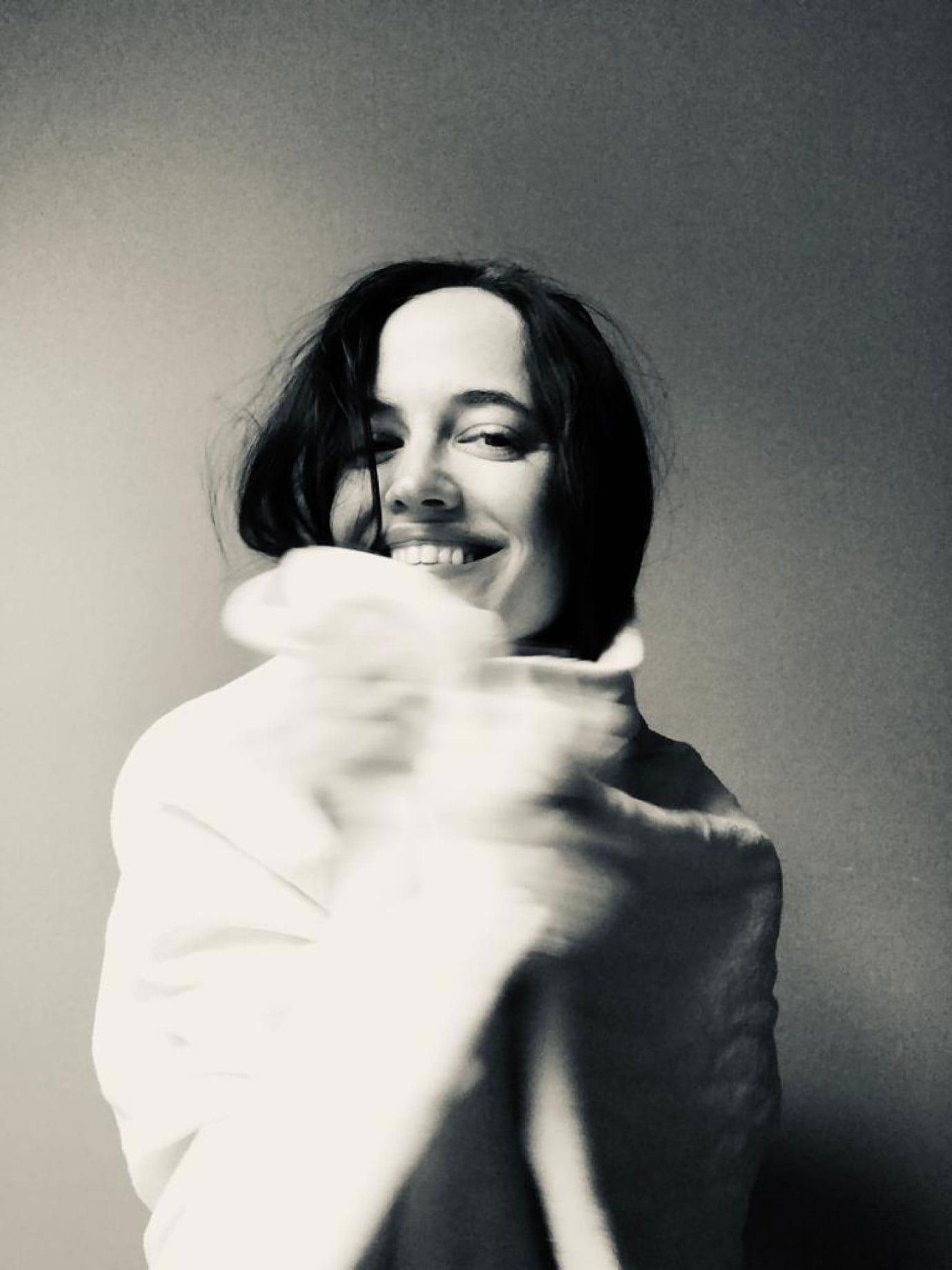 A woman smiling and wrapped in a white blanket.