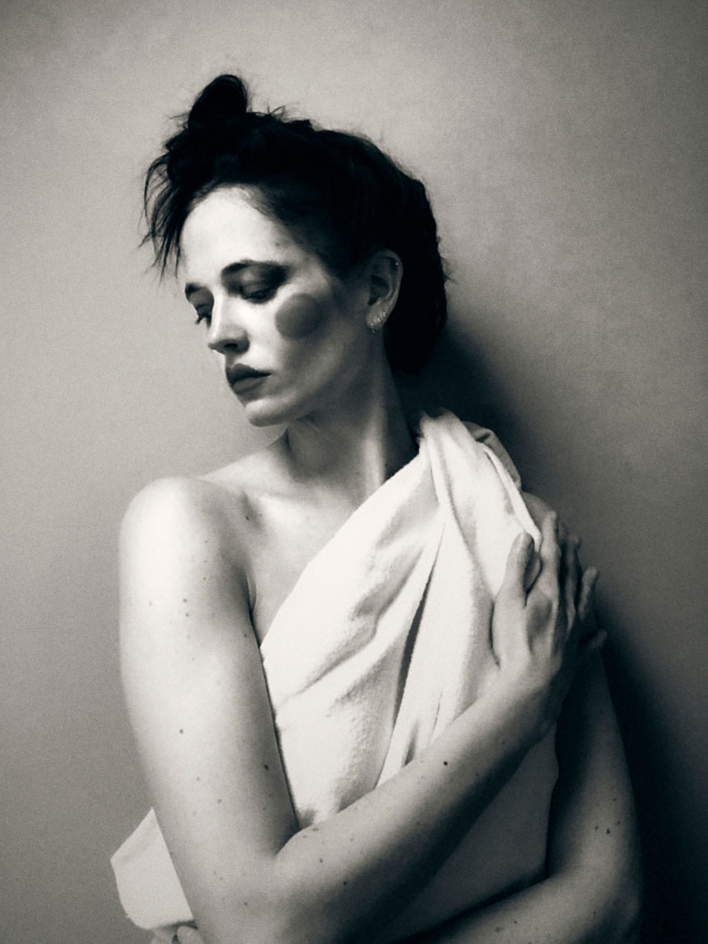 A woman wearing a white blanket with a circle painted on her cheek.