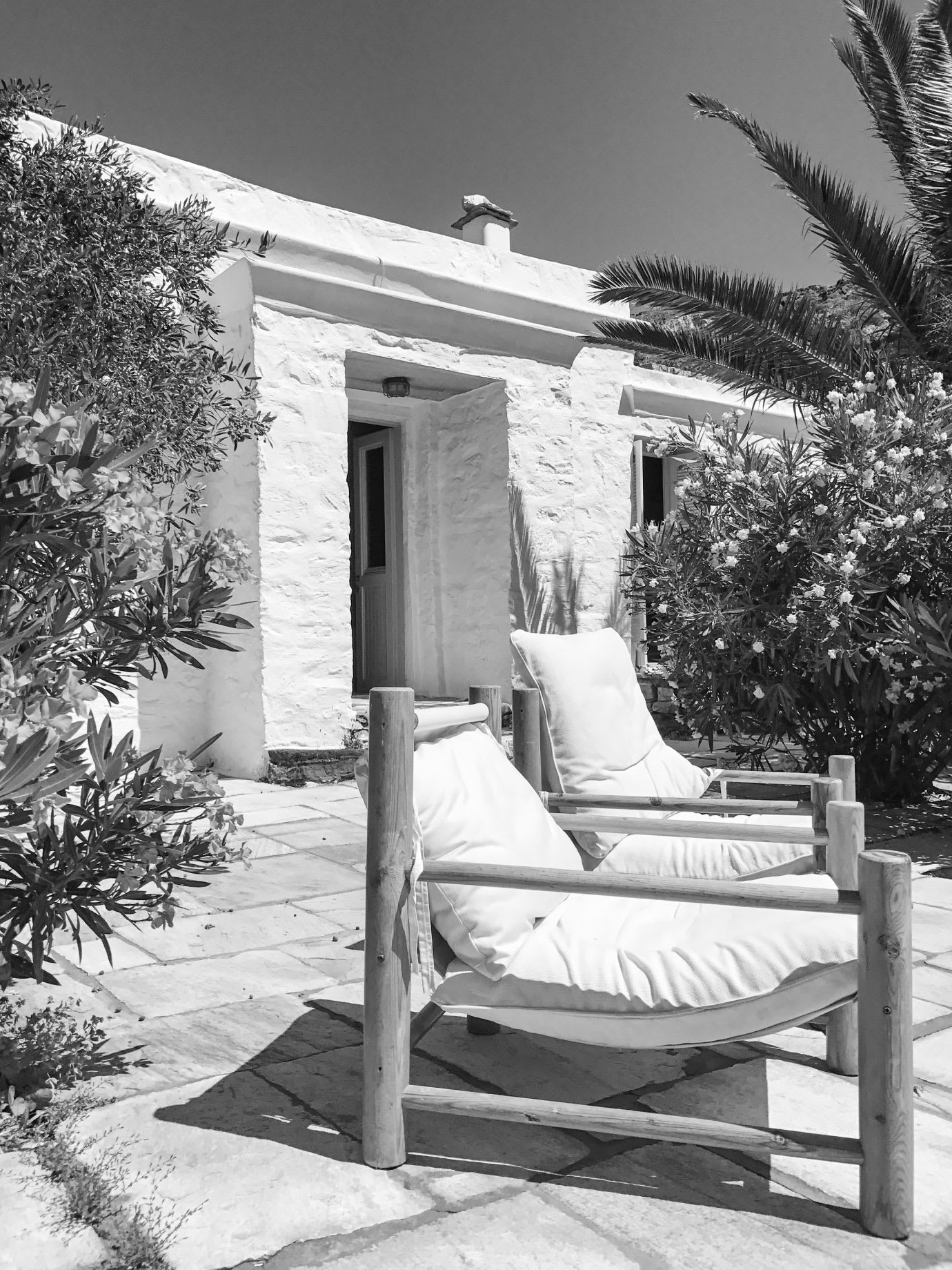 Two outdoor chairs on a terrace by a white house.