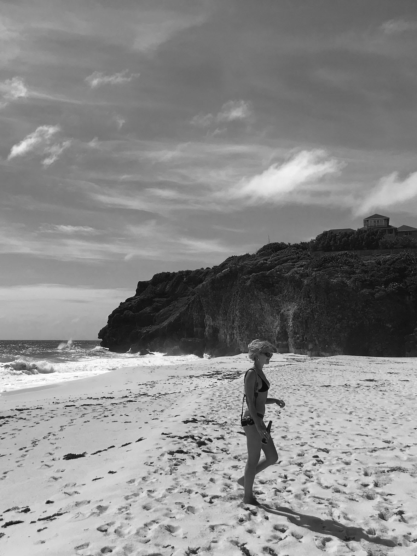 A woman in a bikini walking on a sandy beach.