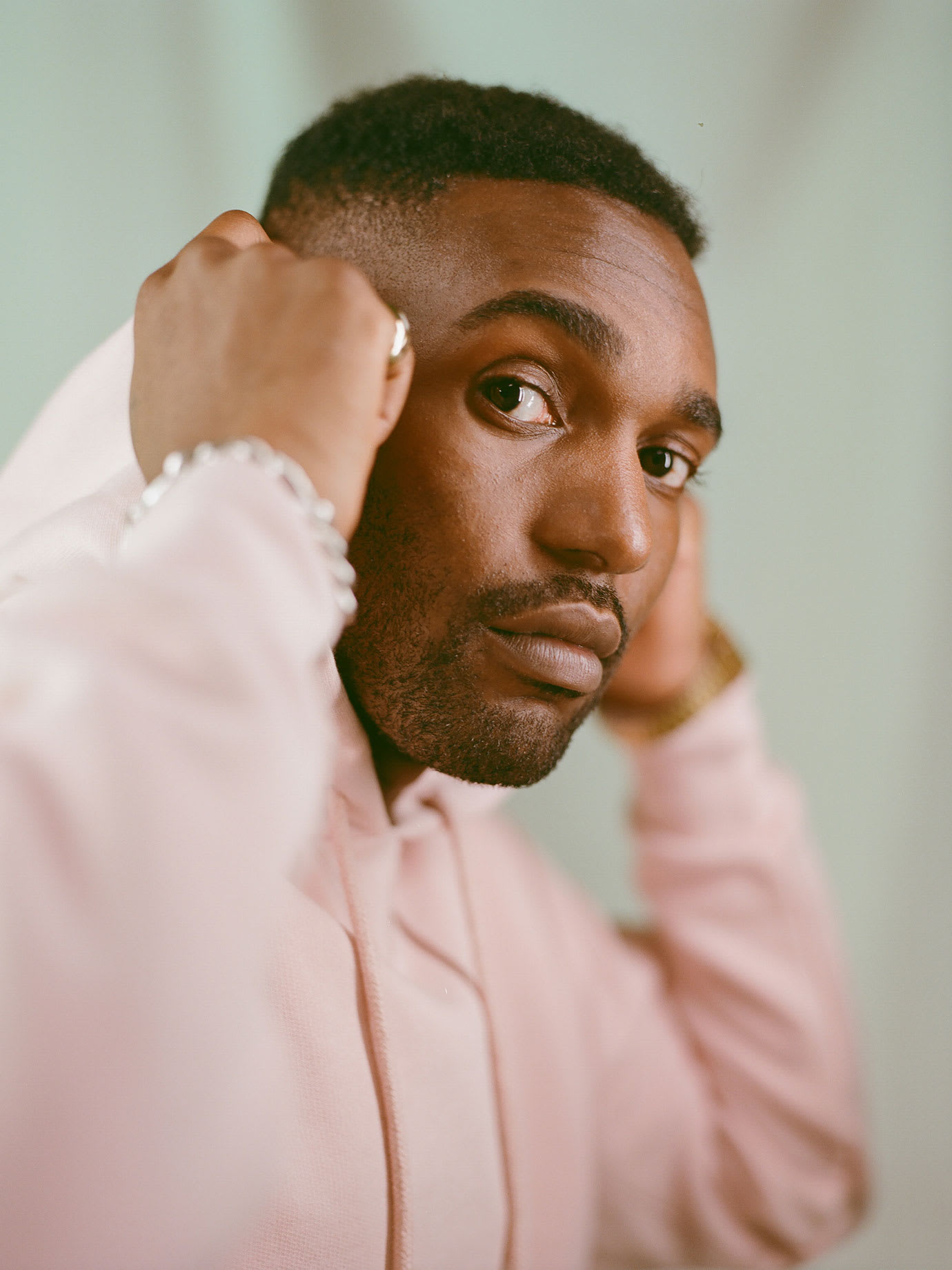 A man wearing a pink hoodie and pulling the hood over his head.