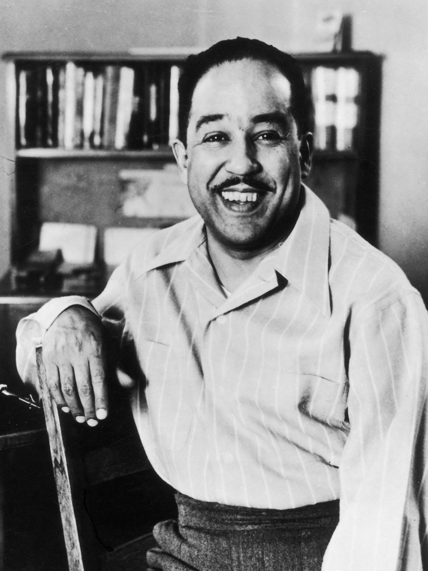 A man smiling with his arm resting on the back of his chair.