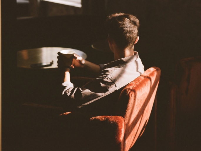 A man drinks while sitting in a red chair.