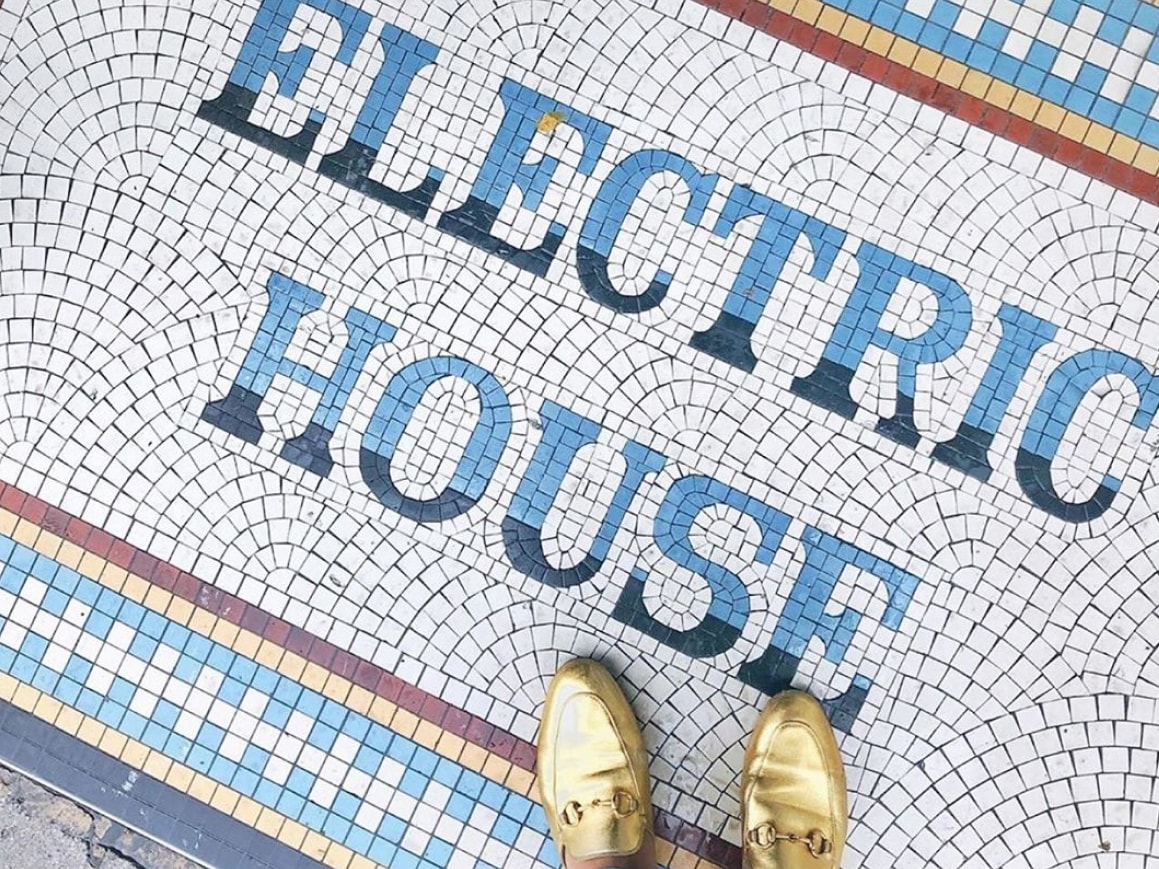 A person wearing gold shoes standing on a mosaic saying Electric House.