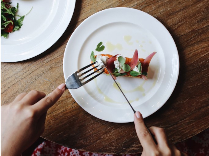 A person cuts into a small plate of salad with a knife and fork.