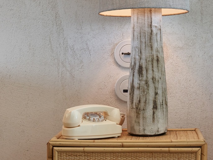 Detail of a bedside table with a telephone and lamp on it.