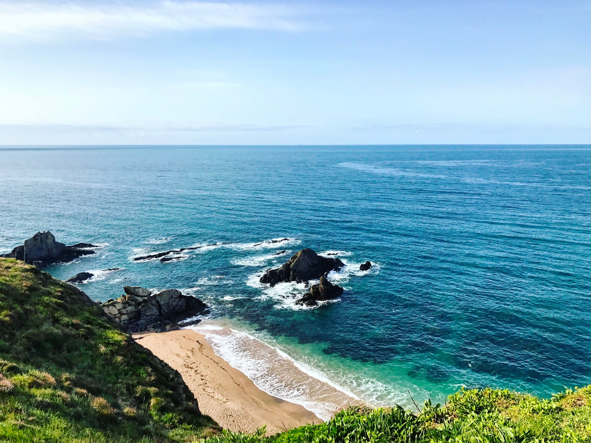A clifftop looking down at a beach and the sea.