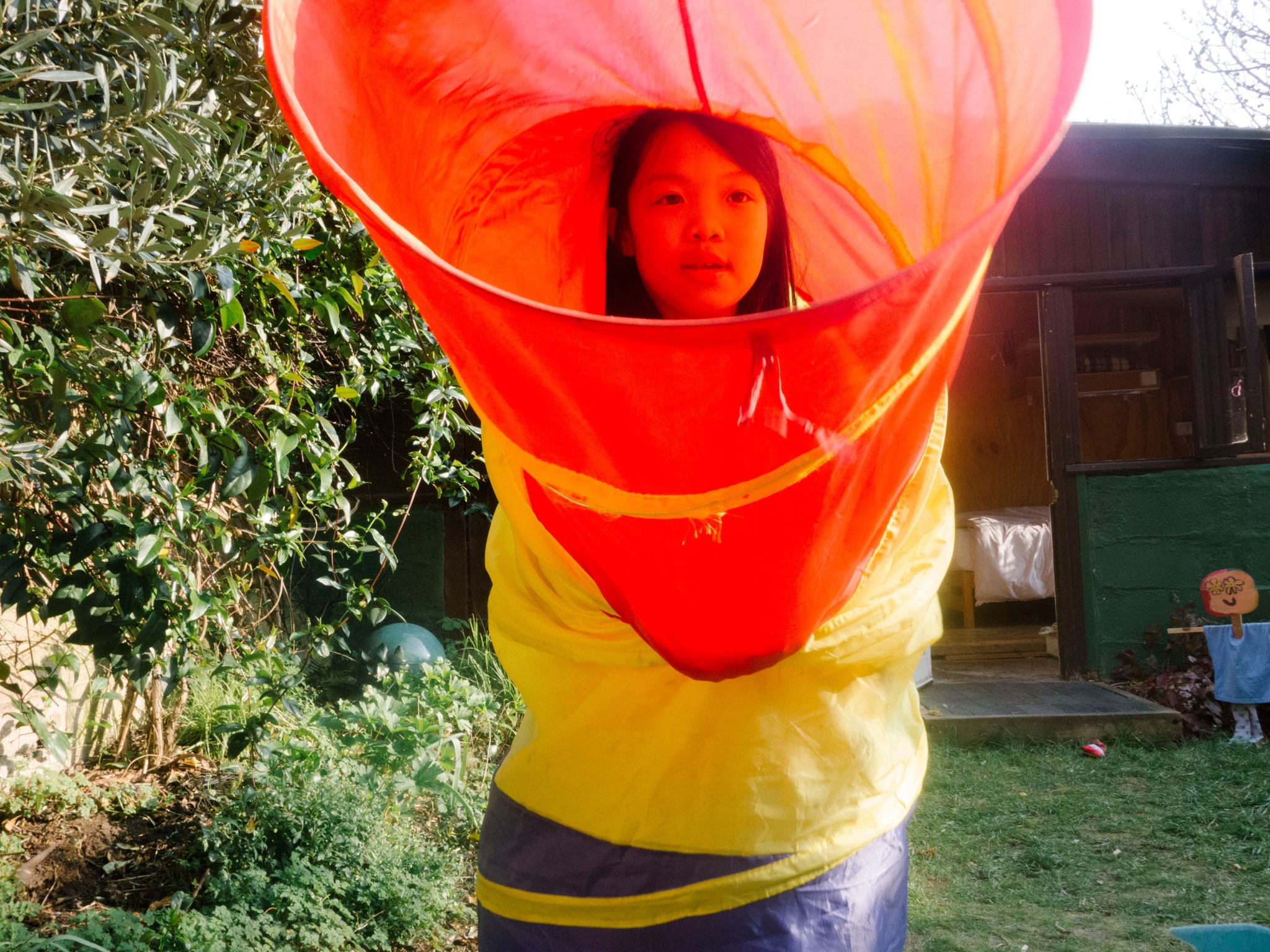 A young girl standing up in a colourful tube in a garden.