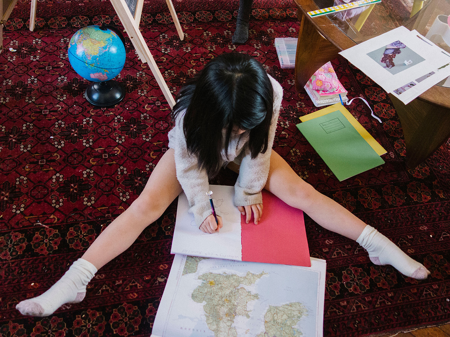 a young girl sitting on the floor with homework and a map