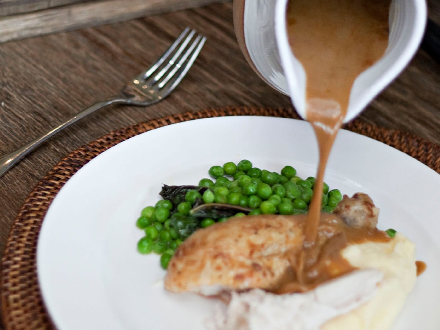 Brown gravy being poured onto a roast chicken lunch.