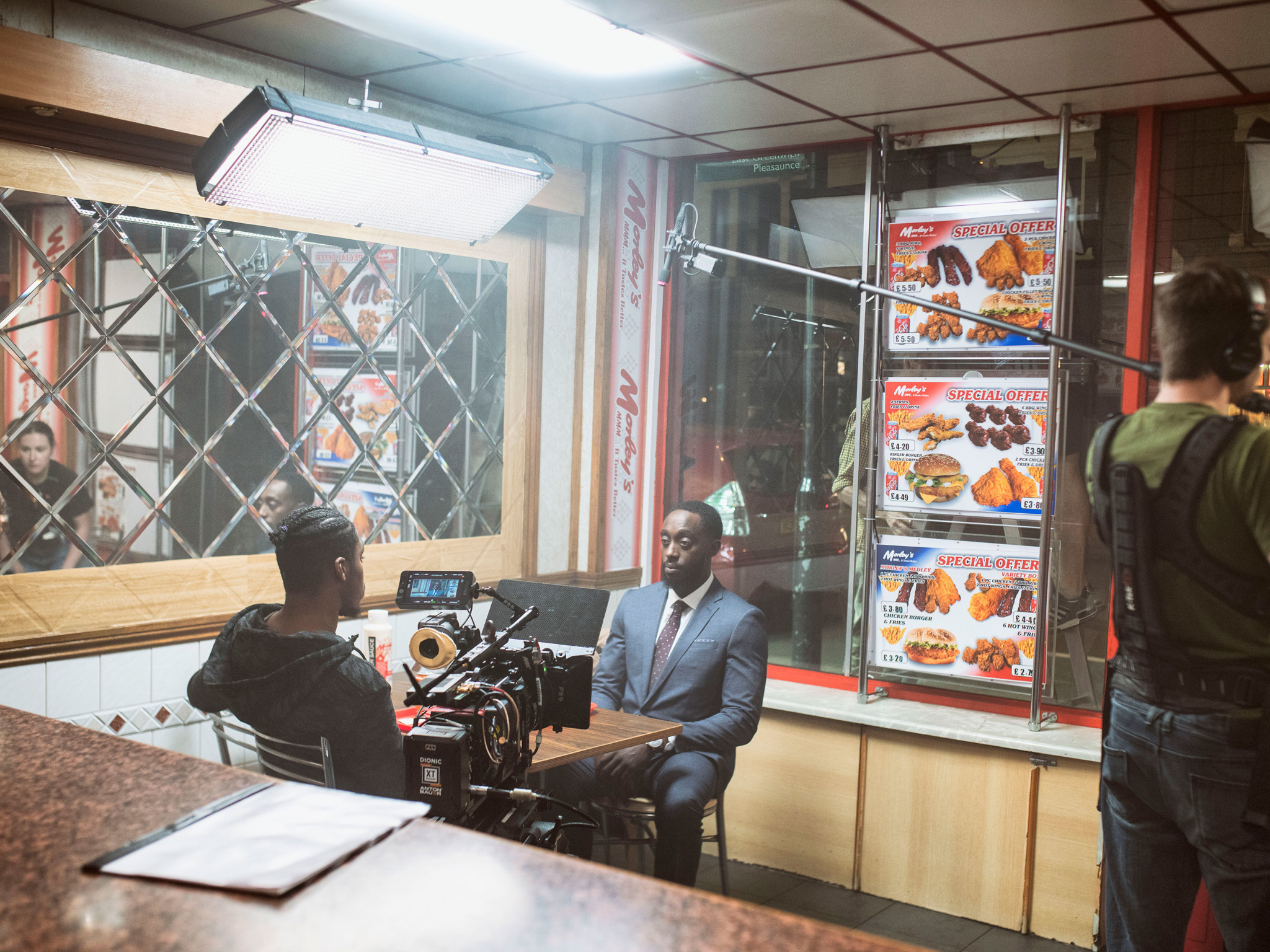 Two men sitting at a table in a chicken shop film set.