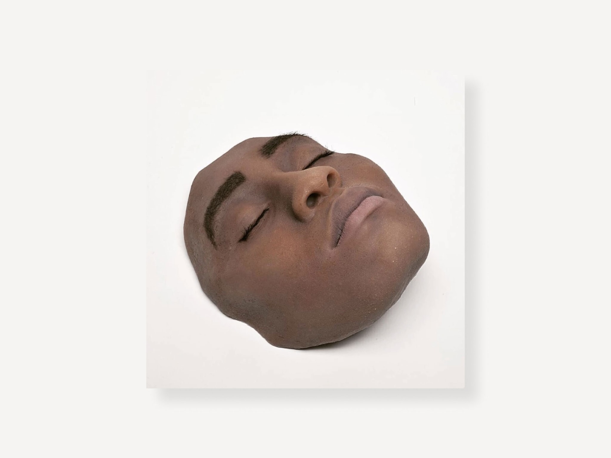 A lifelike sculpture of the front of a person's face on a white block.
