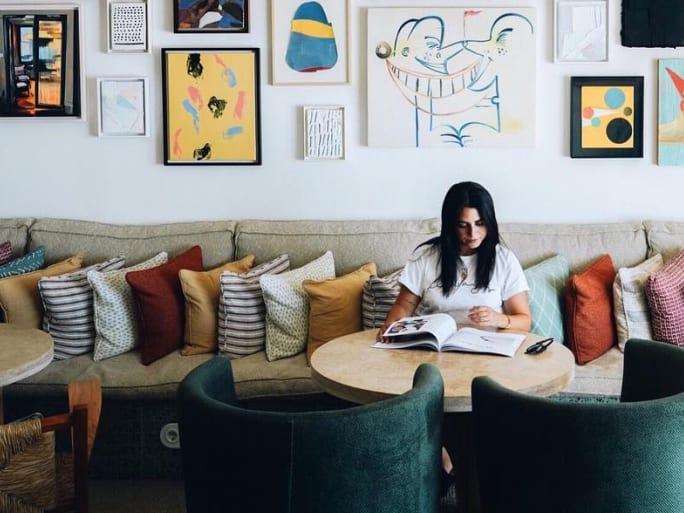 A woman reads on a sofa covered in many cushions