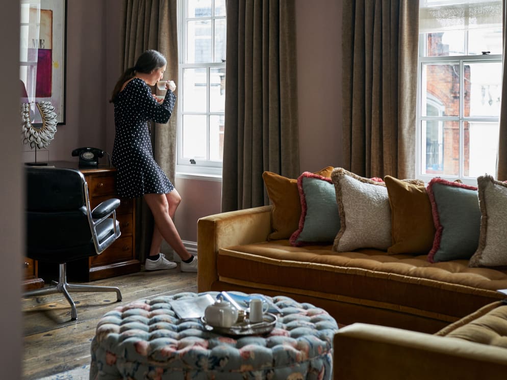 A woman sipping a drink by a window in a lounge-like interior.