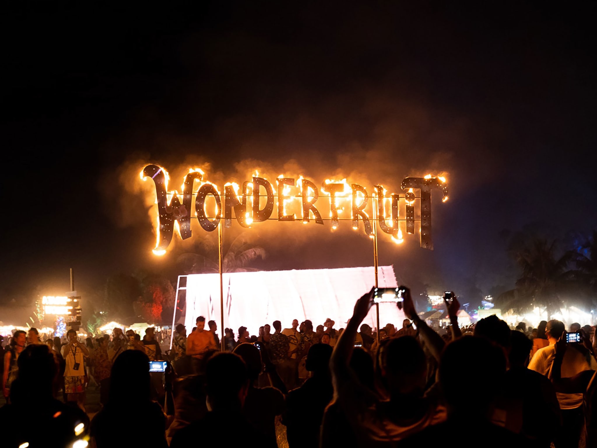 A crowd around a sign with Wonderfruit written in fire on it.