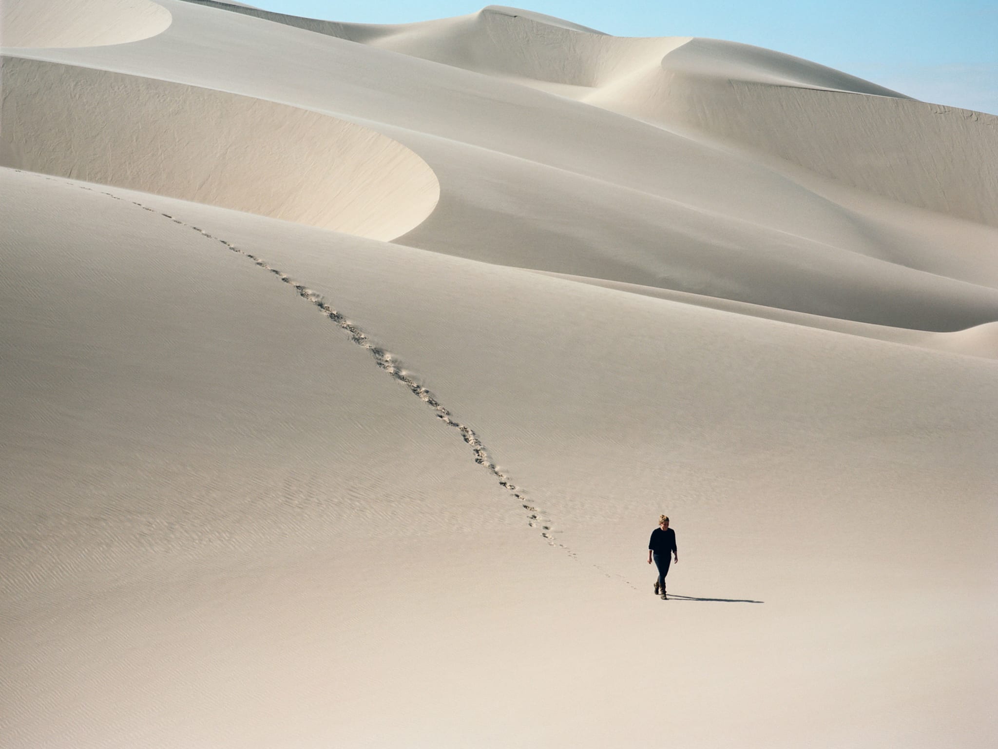 A woman walking on her own over sand dunes with her footprints trailing behind her.