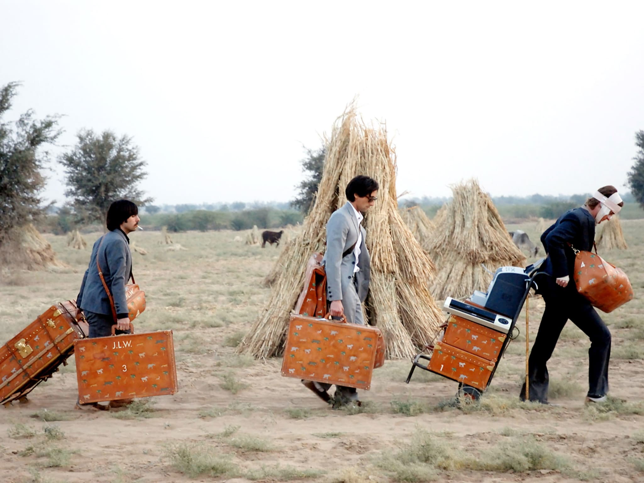 Three men pulling their suitcases through a field.