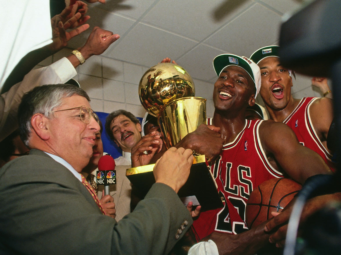 A basketball player holding a trophy with lots of people and cameras around him.