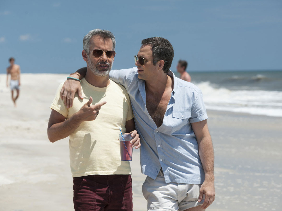 Two men walking on a beach with their arms around each other.