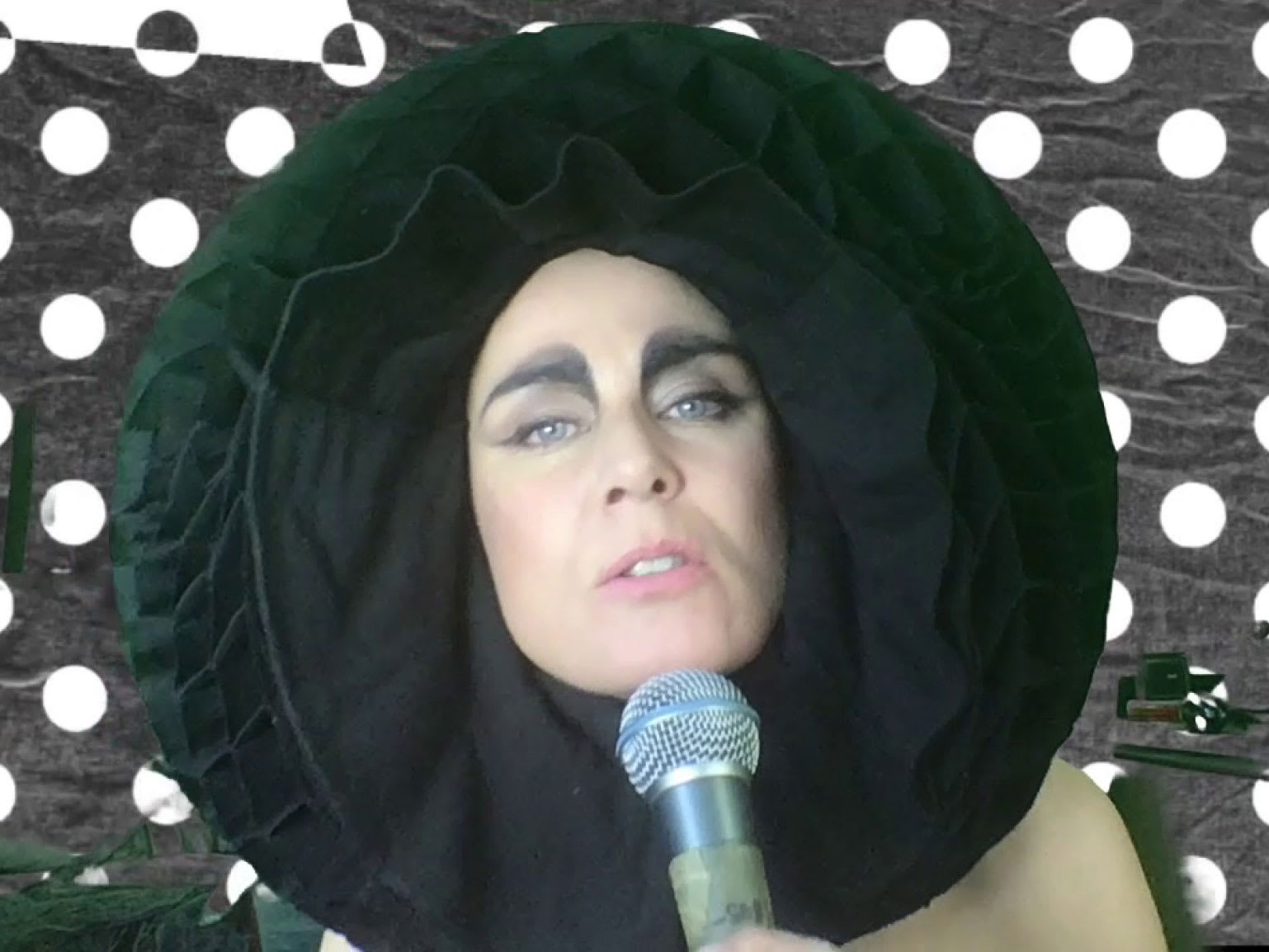 A woman with a wide round head piece and polka dots behind her.