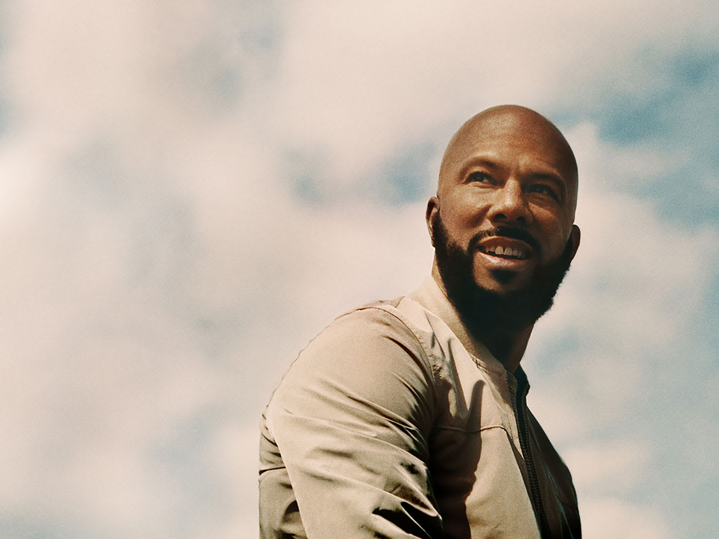 A man smiling under a cloudy blue sky.